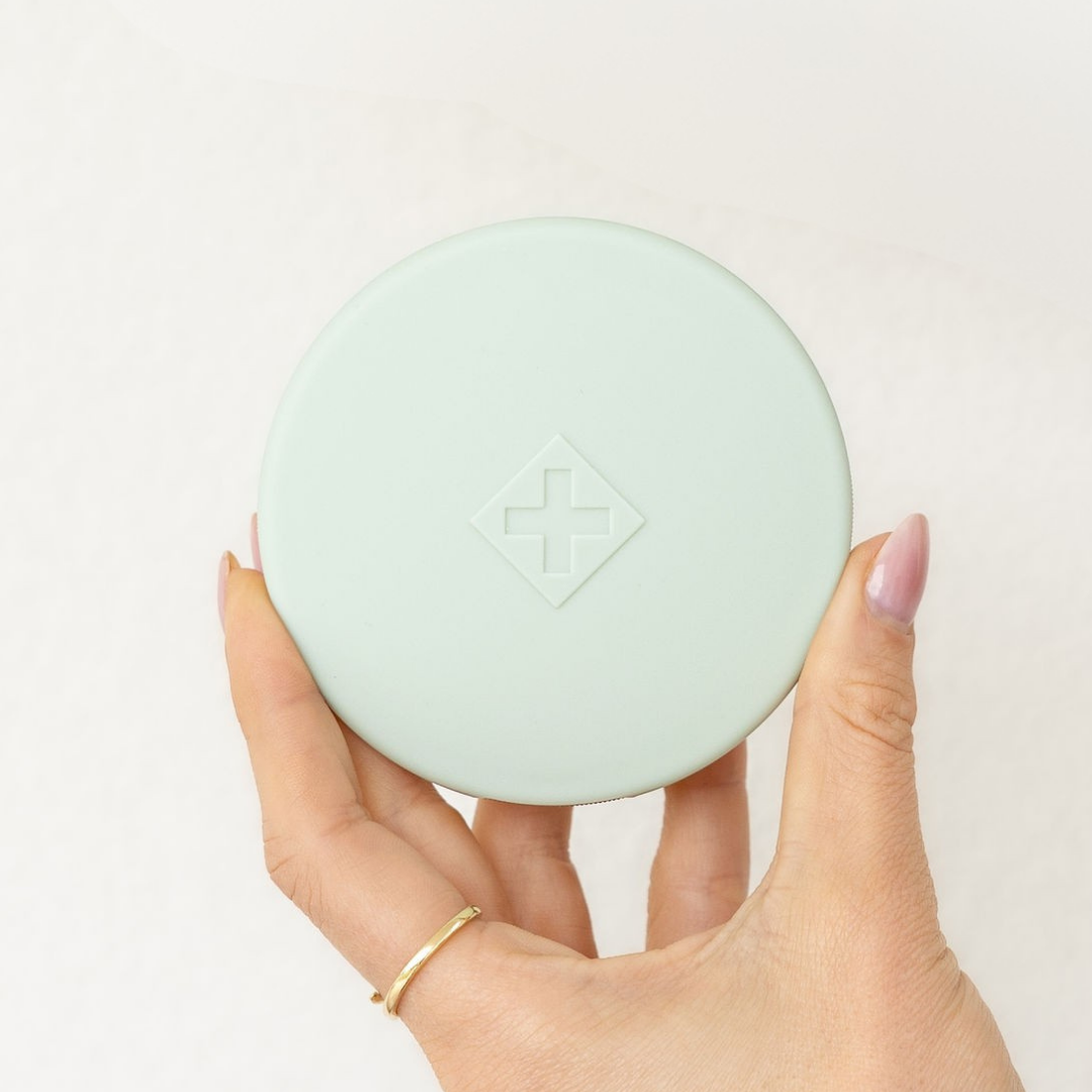 Hand holding a sage Essentials Pill Compact against a white background