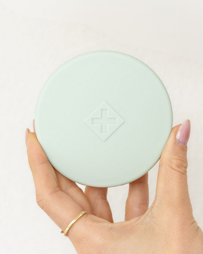 Hand holding a sage Essentials Pill Compact against a white background