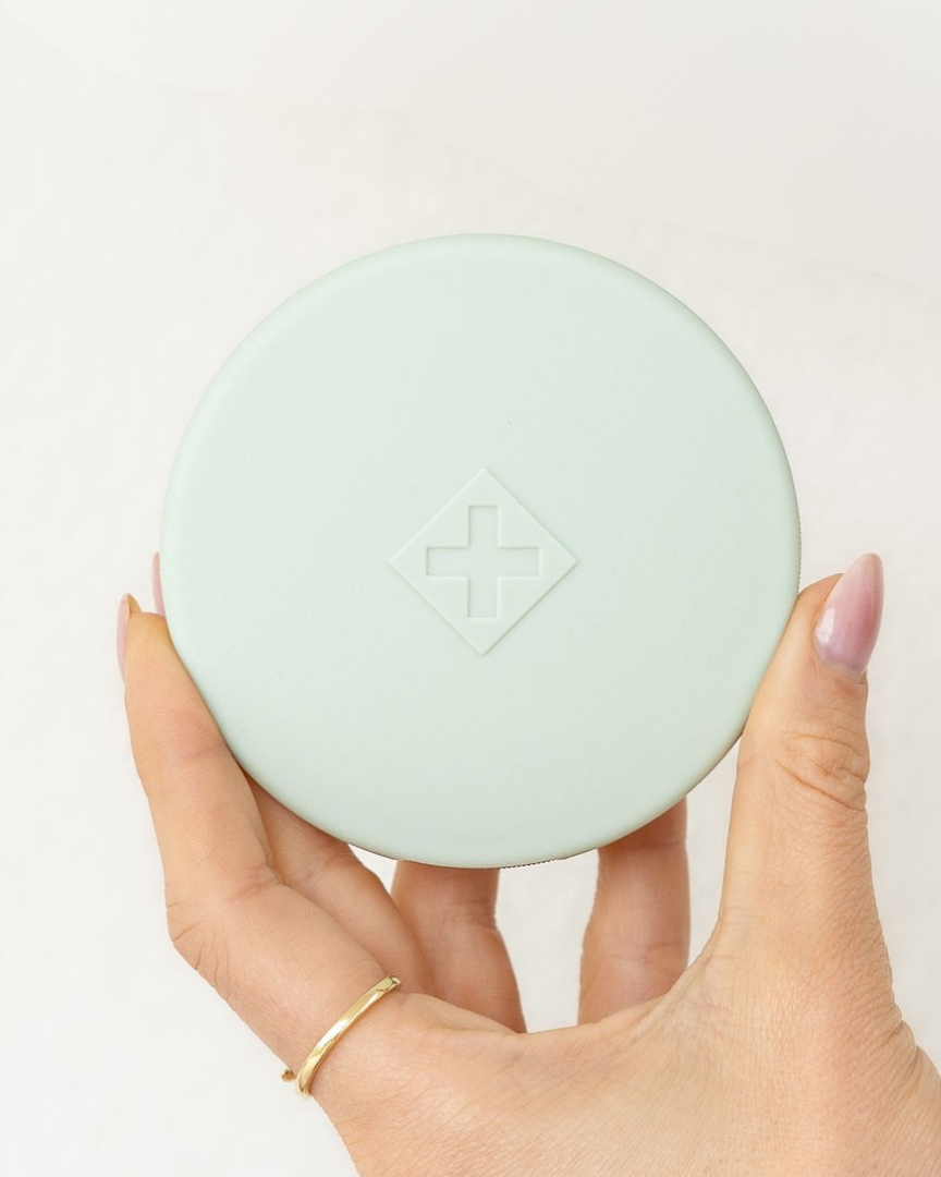 Hand holding a sage Essentials Pill Compact against a white background